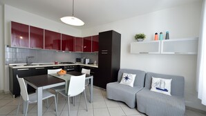 Une cuisine moderne avec des meubles de rangement rouges, un coin repas avec une table et des chaises, et un canapé gris agrémenté de coussins décoratifs.