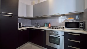 A modern kitchen with dark cabinets, stainless steel appliances, and a microwave on the countertop. - Mina 1 in Gabicce Mare (Cattolica)