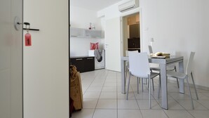 A modern kitchen with white cabinets, a washing machine, and a dining area with a table and chairs. - Mina 1 in Gabicce Mare (Cattolica)