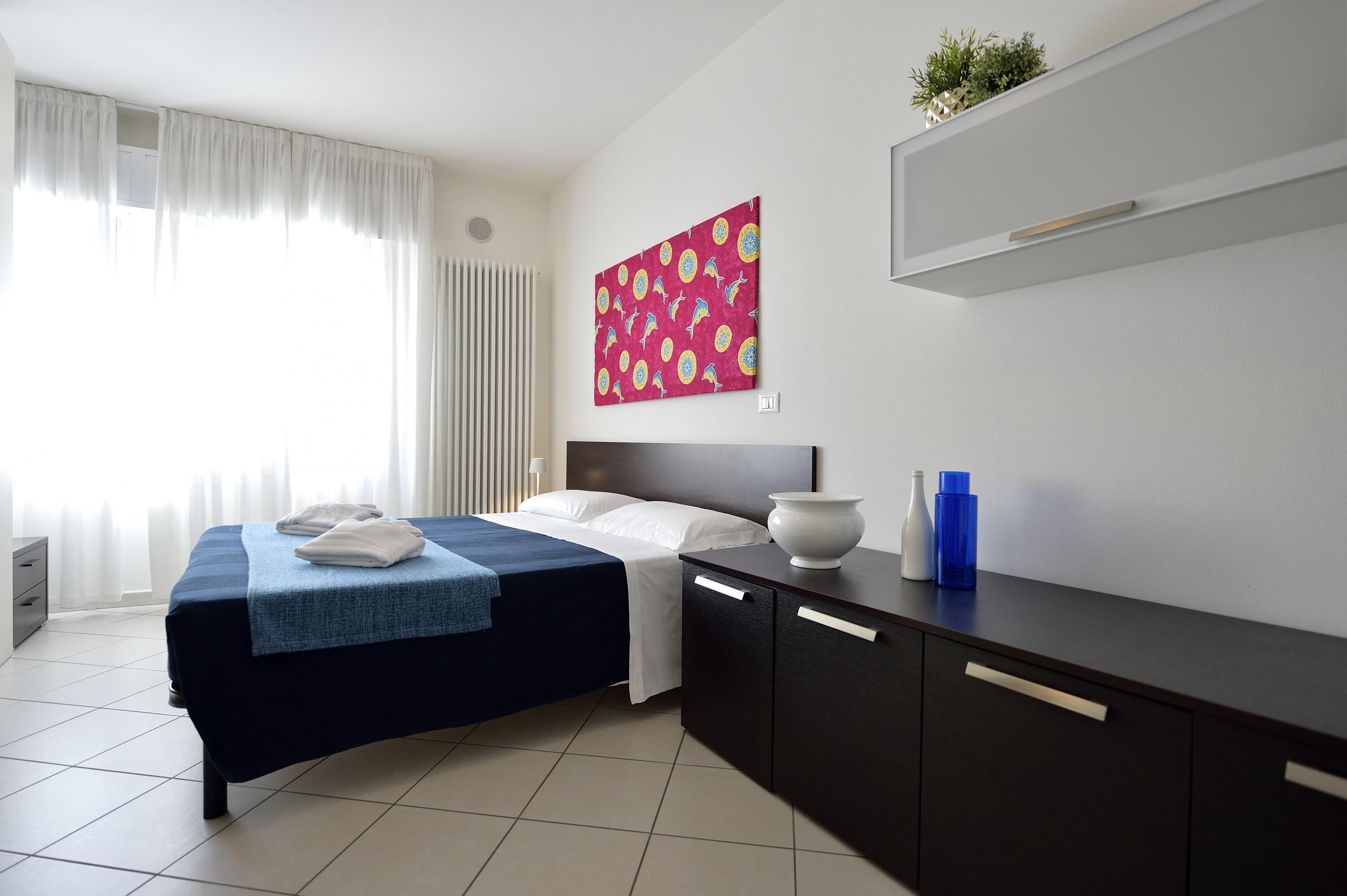 Una habitación de hotel moderna con una cama bien hecha, una mesita de noche con un florero y un estante con adornos.