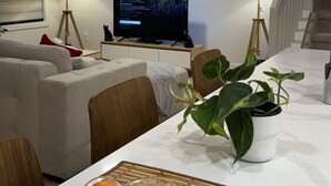 A modern living room with a flat-screen TV, a dining table with a potted plant, and a staircase.