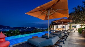 A rooftop infinity pool with lounge chairs and umbrellas, overlooking a cityscape at night. - Samui Summit villa (Koh Samui)