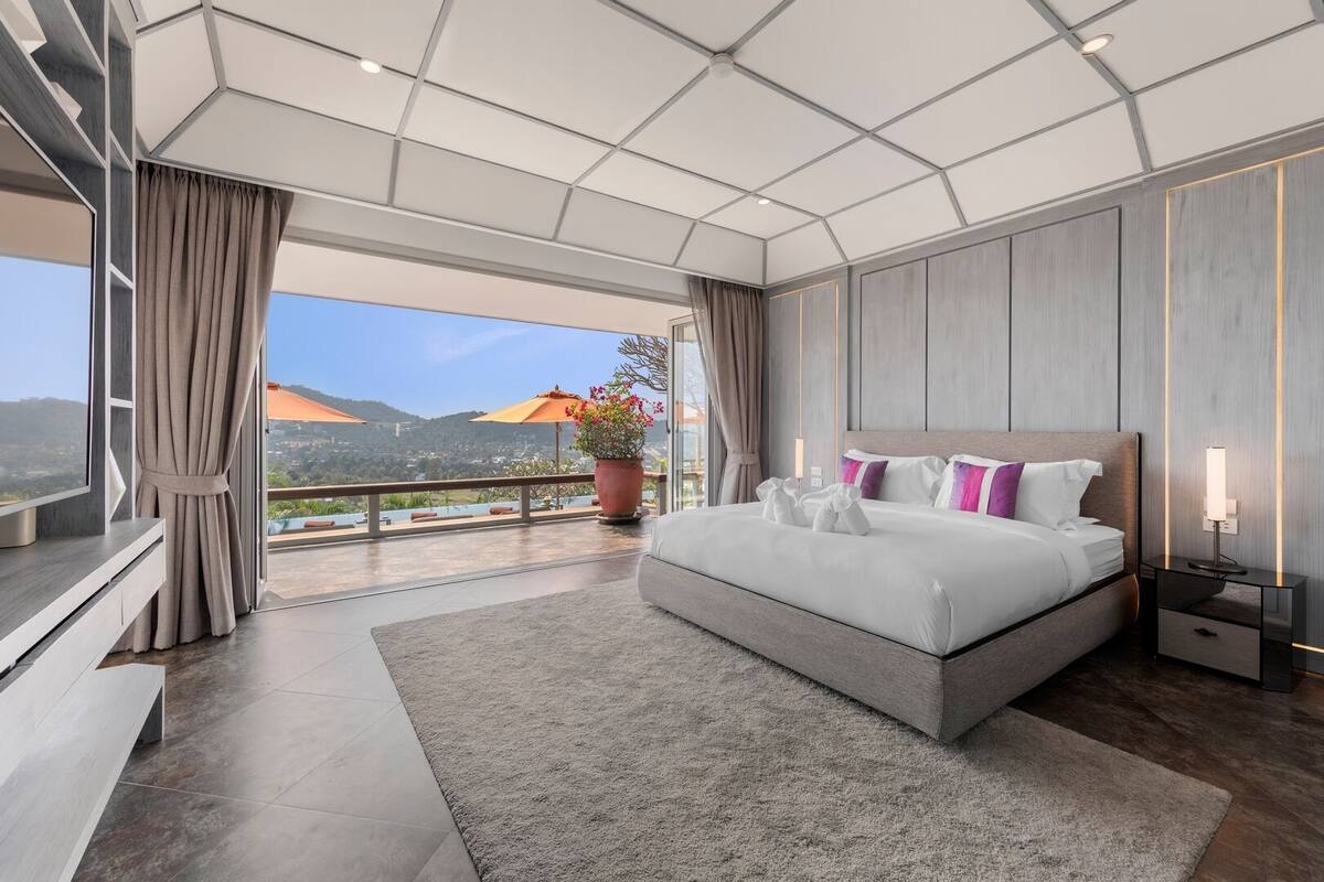 Quarto de hotel moderno com uma cama grande, varanda com vista e uma grande planta em vaso.