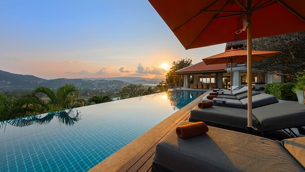 An infinity pool with lounge chairs and umbrellas, overlooking a scenic landscape with mountains and a sunset. - Samui Summit villa (Koh Samui)