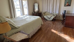 Een slaapkamer met een bed, een stoel, een dressoir, een spiegel en een plafondventilator.
