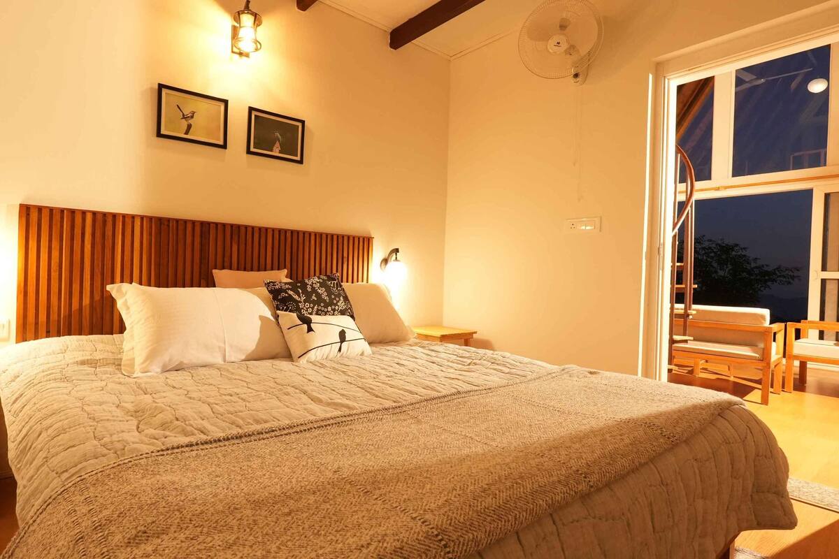 A bedroom with a large bed, wooden headboard, two wall-mounted lights, and a window with a view.