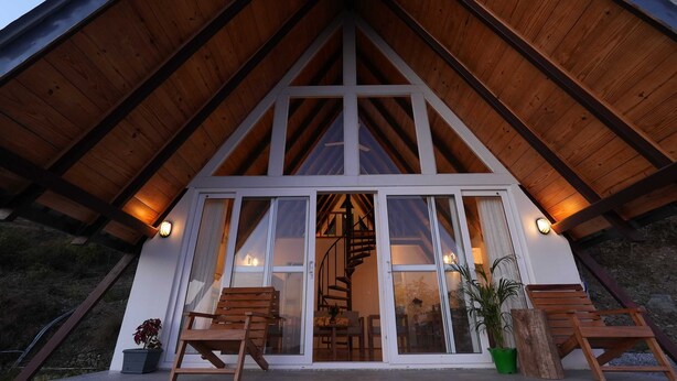 Un chalet en bois doté d’un toit à forte pente, d’un escalier en colimaçon et d’une grande porte-fenêtre coulissante donnant sur un intérieur comprenant un coin repas.