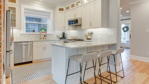Une cuisine moderne avec des meubles blancs, un îlot central doté de tabourets, un lave-vaisselle en acier inoxydable et un four à micro-ondes.