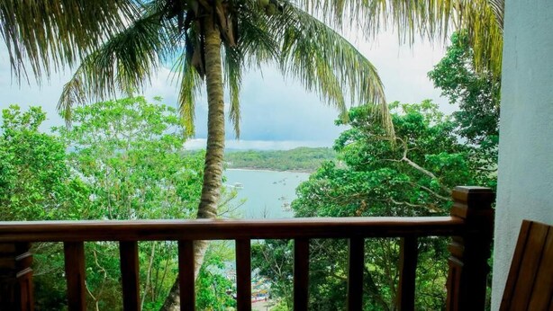 Un balcón de madera con vistas a un paisaje tropical, que incluye un cuerpo de agua y vegetación densa.