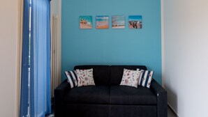 Ein Zimmer mit einer schwarzen Couch, einer blauen Wand und einer gelben Deckenleuchte.