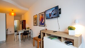 Ein modernes Wohnzimmer mit Essbereich, einem Holztisch und einem an der Wand befestigten Fernseher.