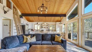 A spacious living area with a large sectional sofa, a wooden coffee table, and a kitchen in the background. - Timber Peak Cabin! Hot Tub,BBQ & Scenic Views! (Divide)