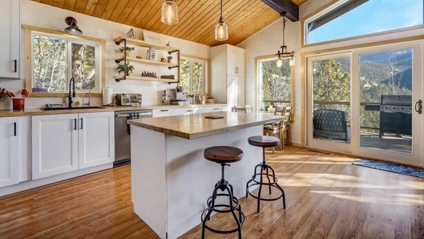 A spacious kitchen with wooden cabinets, a large island, pendant lighting, and a view of the outdoors through large sliding glass doors. - Timber Peak Cabin! Hot Tub,BBQ & Scenic Views! (Divide)
