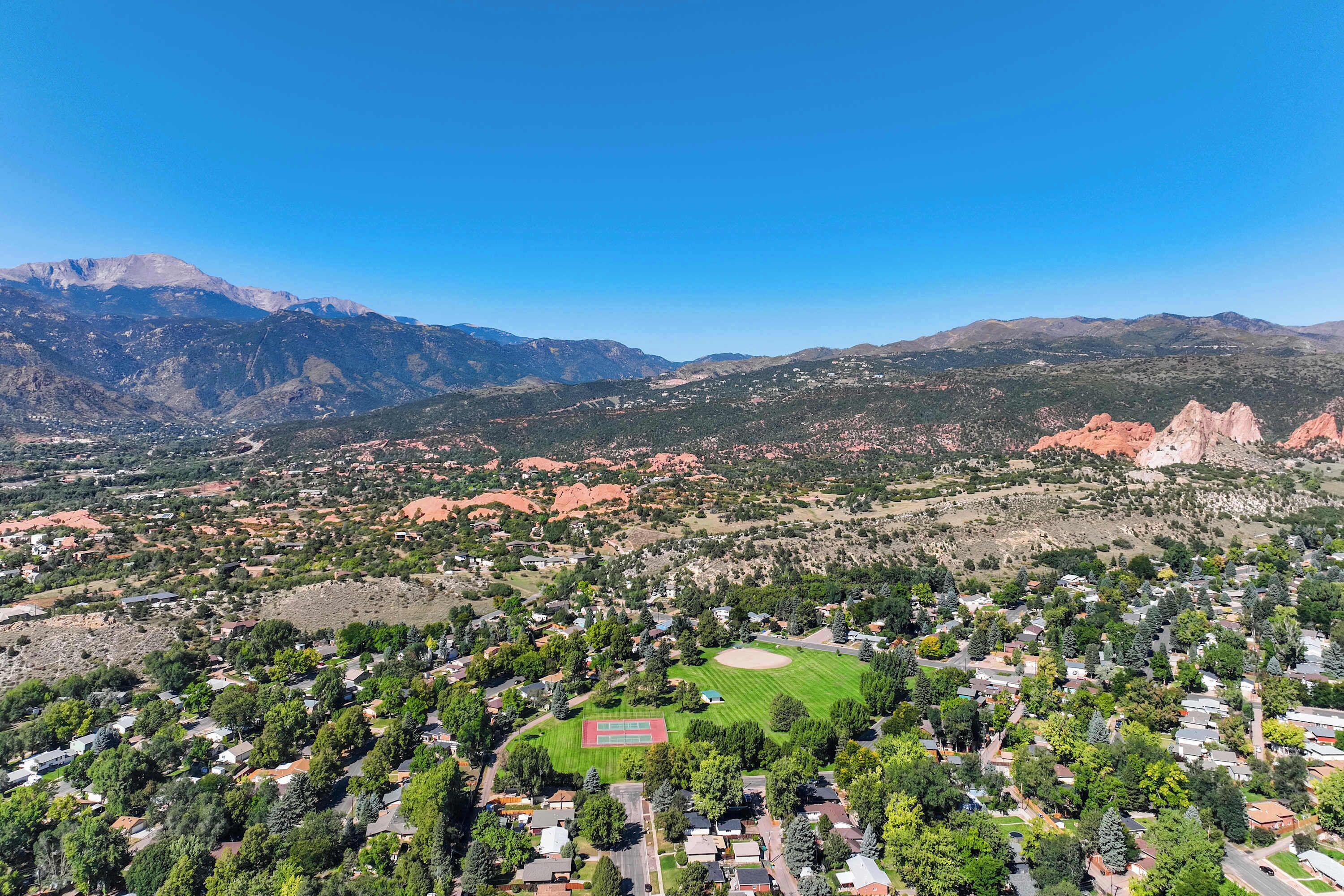 An aerial view of a residential area with houses, a green park, and mountains in the background.