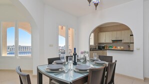 A dining area with a table set for four, a kitchen visible through an archway, and large windows offering a view. - Wonderful and comfortable villa  with private pool in Benitachell, Costa Blanca, Spain for 6 persons (Benitachell)