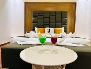 A hotel room with a bed, two drinks on a table, and a wooden headboard. - Aravalli Hill Resort (Chittorgarh)