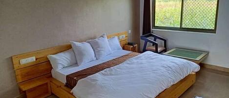 Une chambre avec un lit simple, une tête de lit en bois, du linge de lit blanc, une petite table de chevet et une fenêtre donnant sur un paysage verdoyant.