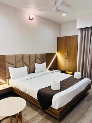 A modern hotel room with a large bed, a bedside table, a small round table, and a wardrobe. - Aravalli Hill Resort (Chittorgarh)