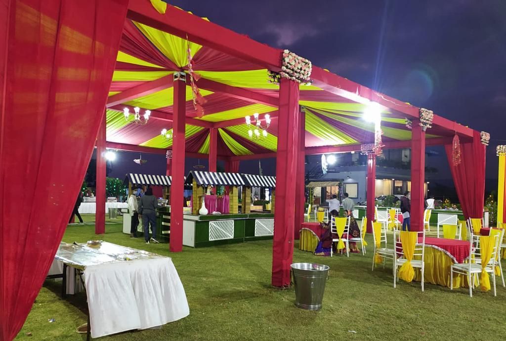 An outdoor event space with a covered area, tables, chairs, and a grassy lawn.