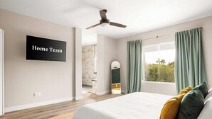 A bedroom with a bed, a ceiling fan, a TV on the wall, and a window with curtains. - Private Pickleball Court, Movie Room, & Hot Tub! (Scottsdale)