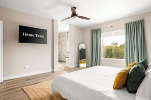 A bedroom with a bed, a ceiling fan, a TV on the wall, and a window with curtains.