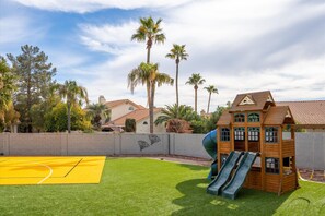 Un terrain de jeux avec des toboggans et un terrain de basket, entouré de palmiers et de maisons.
