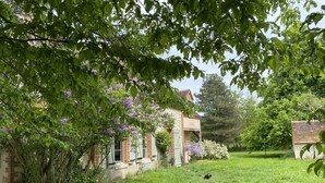 Ein rustikales Steinhaus mit Garten, umgeben von üppigem Grün und blühenden Bäumen.