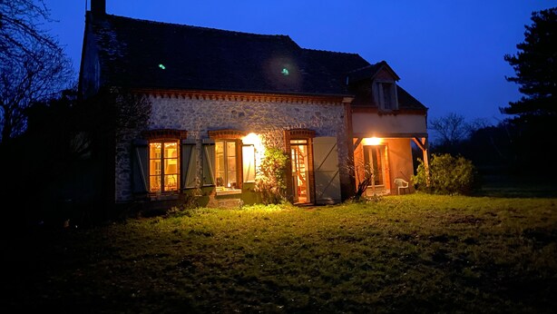 Ein Haus aus Stein mit Ziegeldach, zahlreichen Fenstern und einer gut beleuchteten Veranda.