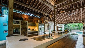 A spacious kitchen with a large island, a brick wall, and a wooden ceiling.
