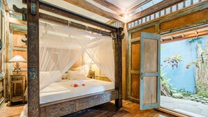 A four-poster bed with a canopy, wooden floor, and a view of a garden through an open door.