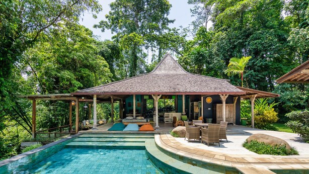 A pool area with a covered seating area and lounge chairs.