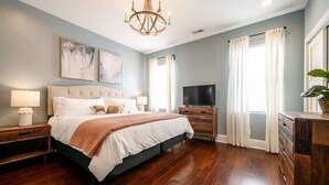 Une chambre à coucher avec un grand lit, une télévision, une commode et un lustre.