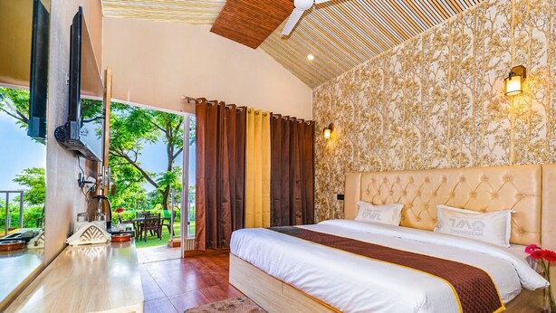 A bedroom with a large bed, a TV, and a view of the outdoors. - The Bluewind Resort (Dehradun)