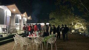 An outdoor dining area with tables and chairs, surrounded by trees and a building with a lighted exterior. - The Bluewind Resort (Dehradun)