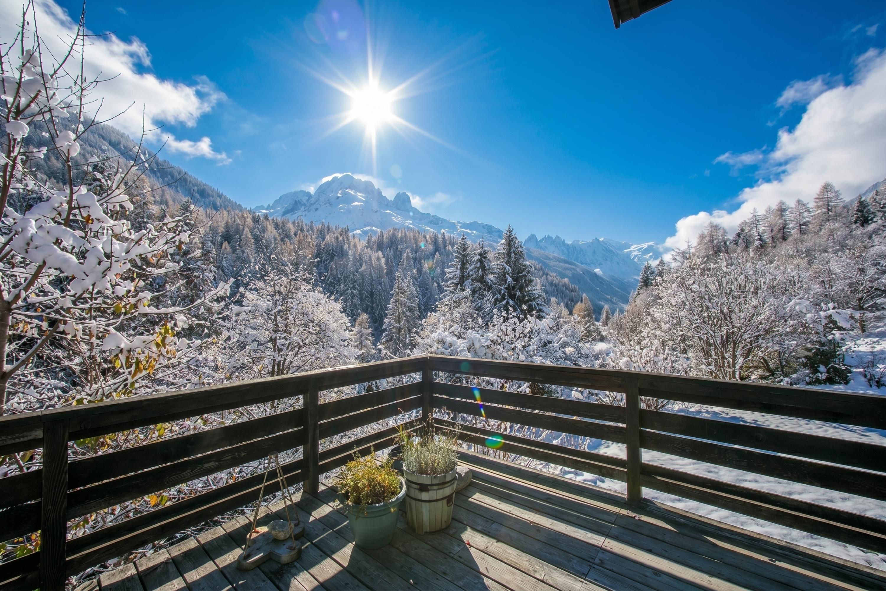 Een houten terras met uitzicht op besneeuwde bergen en een stralende zon.