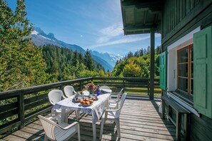 A wooden deck with a table set for dining, overlooking a mountainous landscape.