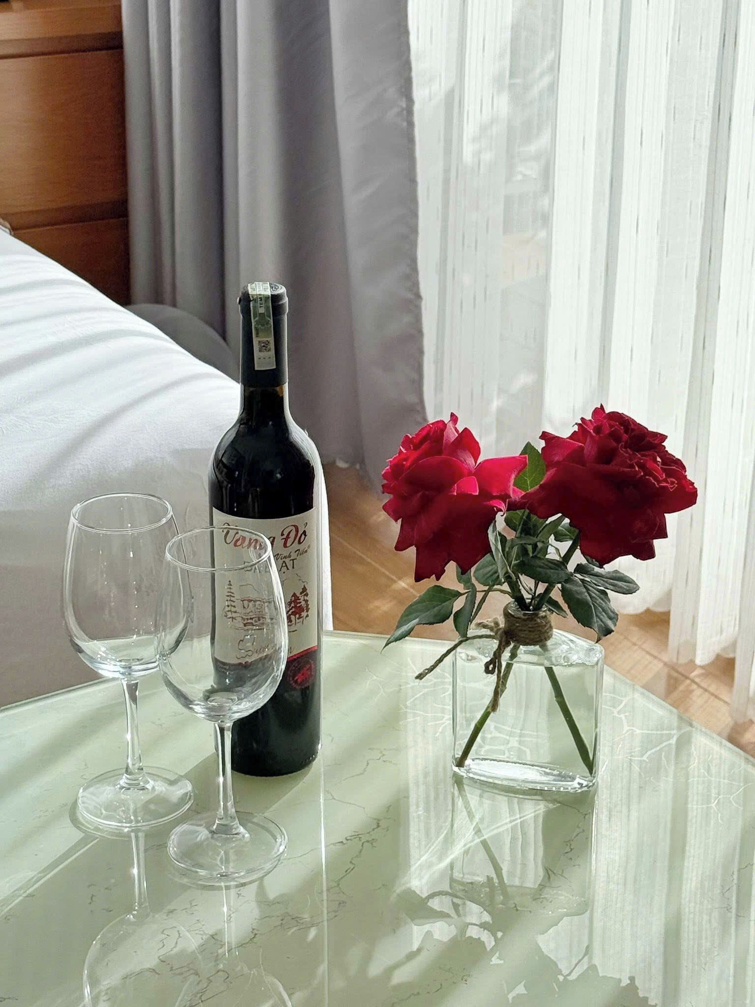 A table with a wine bottle, two wine glasses, and a vase with red roses.