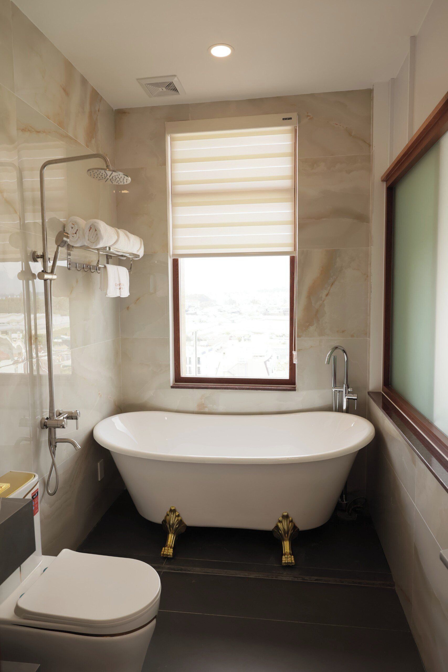 A bathroom with a freestanding bathtub, a toilet, and a window with blinds.
