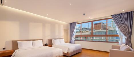 A hotel room with two beds, a sofa, a large window with a view of a building, and wooden flooring.