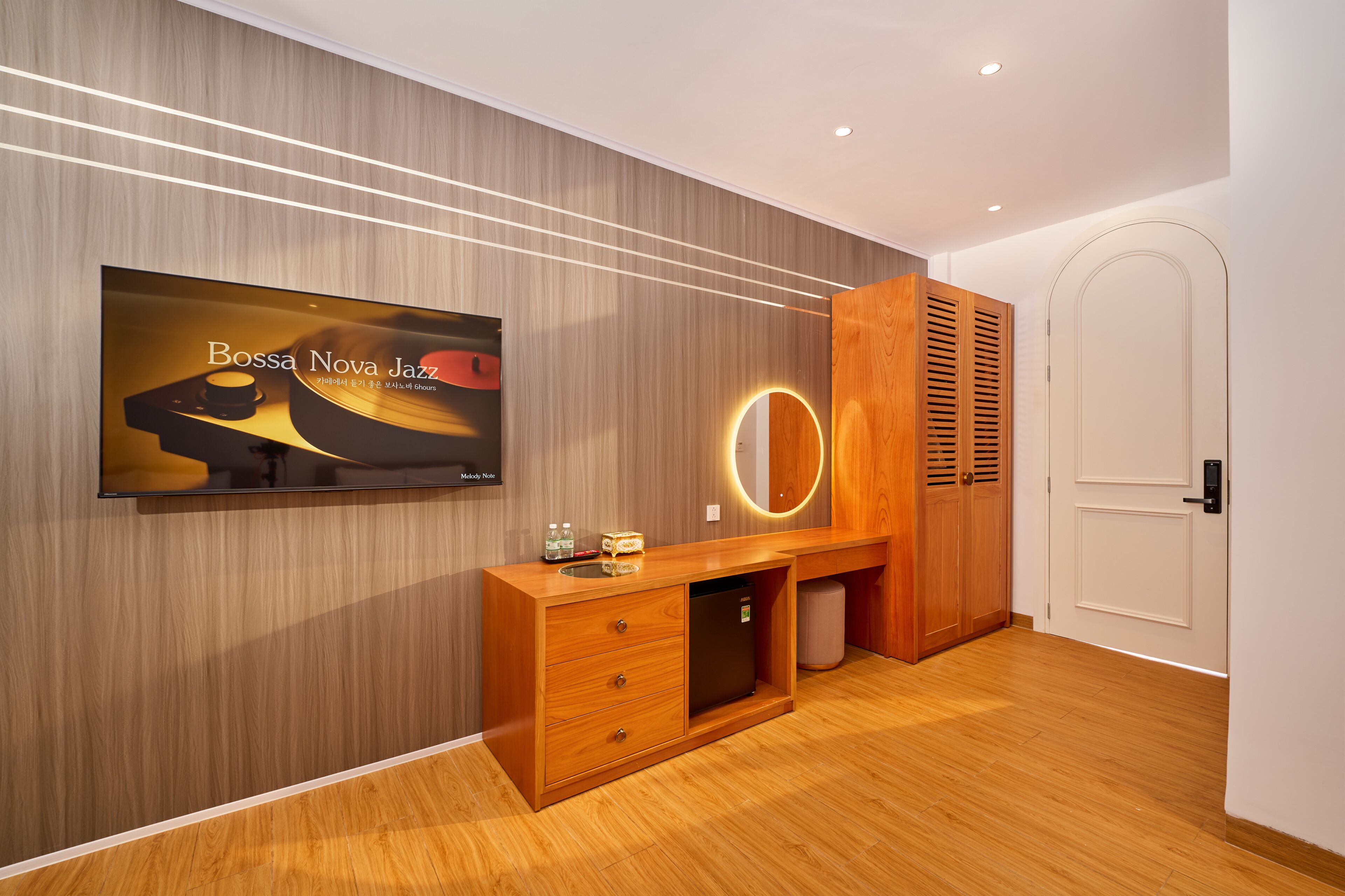 Une chambre moderne avec une coiffeuse en bois, un téléviseur fixé au mur et une porte dotée d’un luminaire circulaire.