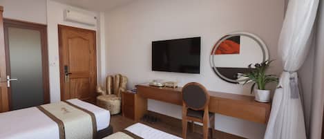 A hotel room with two beds, a desk, a chair, a TV, a mirror, and a potted plant.