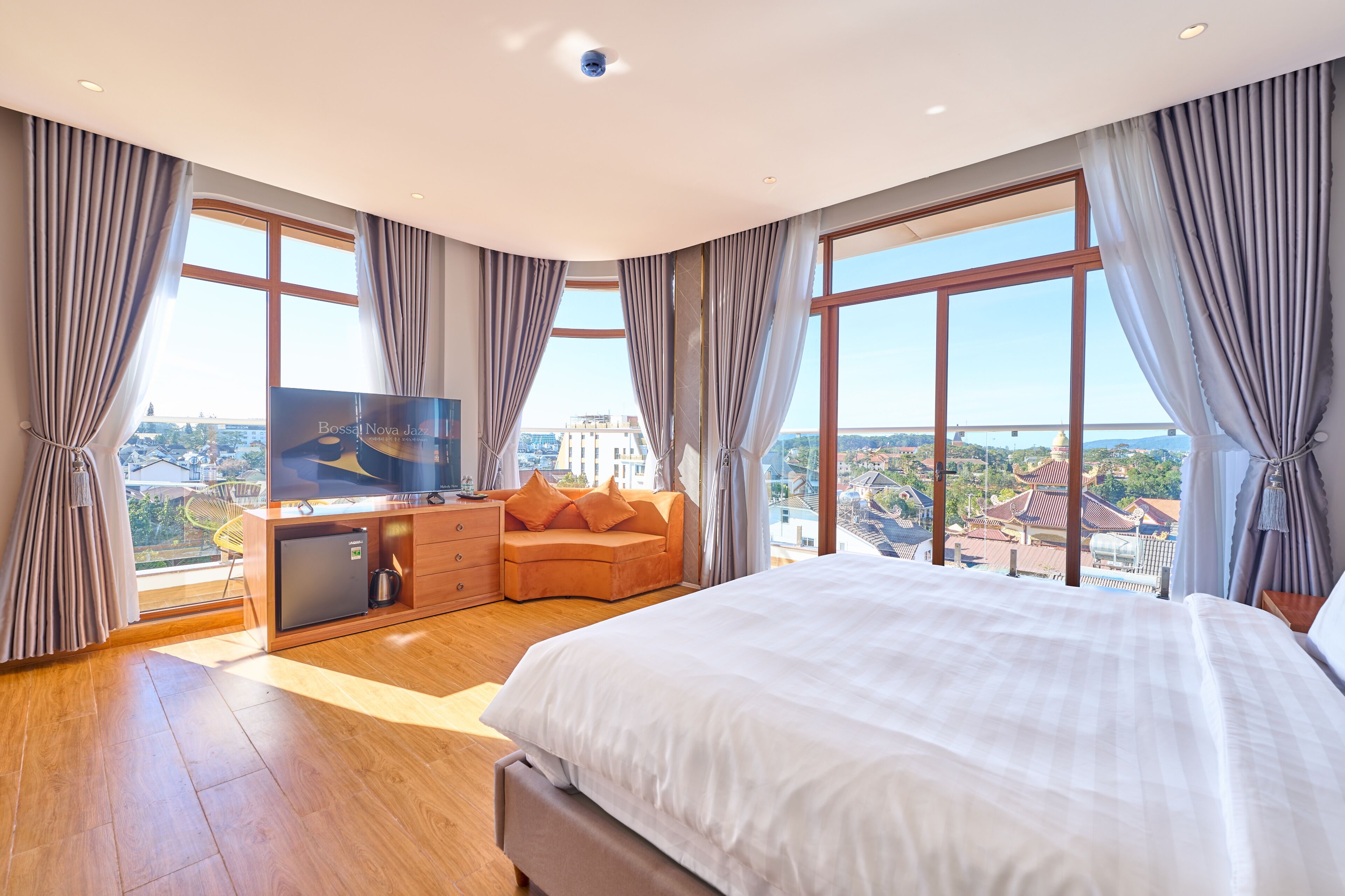 Ein modernes Hotelzimmer mit einem großen Bett, einem Fernseher, einem kleinen Schreibtisch und Blick auf die Stadt.