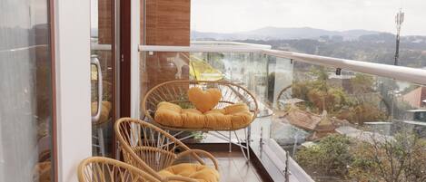 A balcony with wicker chairs and cushions, a glass railing, and a view of the cityscape.