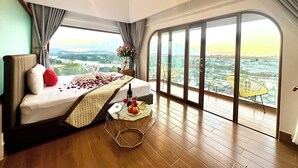 A bedroom with a bed, a small table with a bottle and glasses, and a balcony with a view. - Cat Tuong Hotel (Lam Vien - Da Lat)