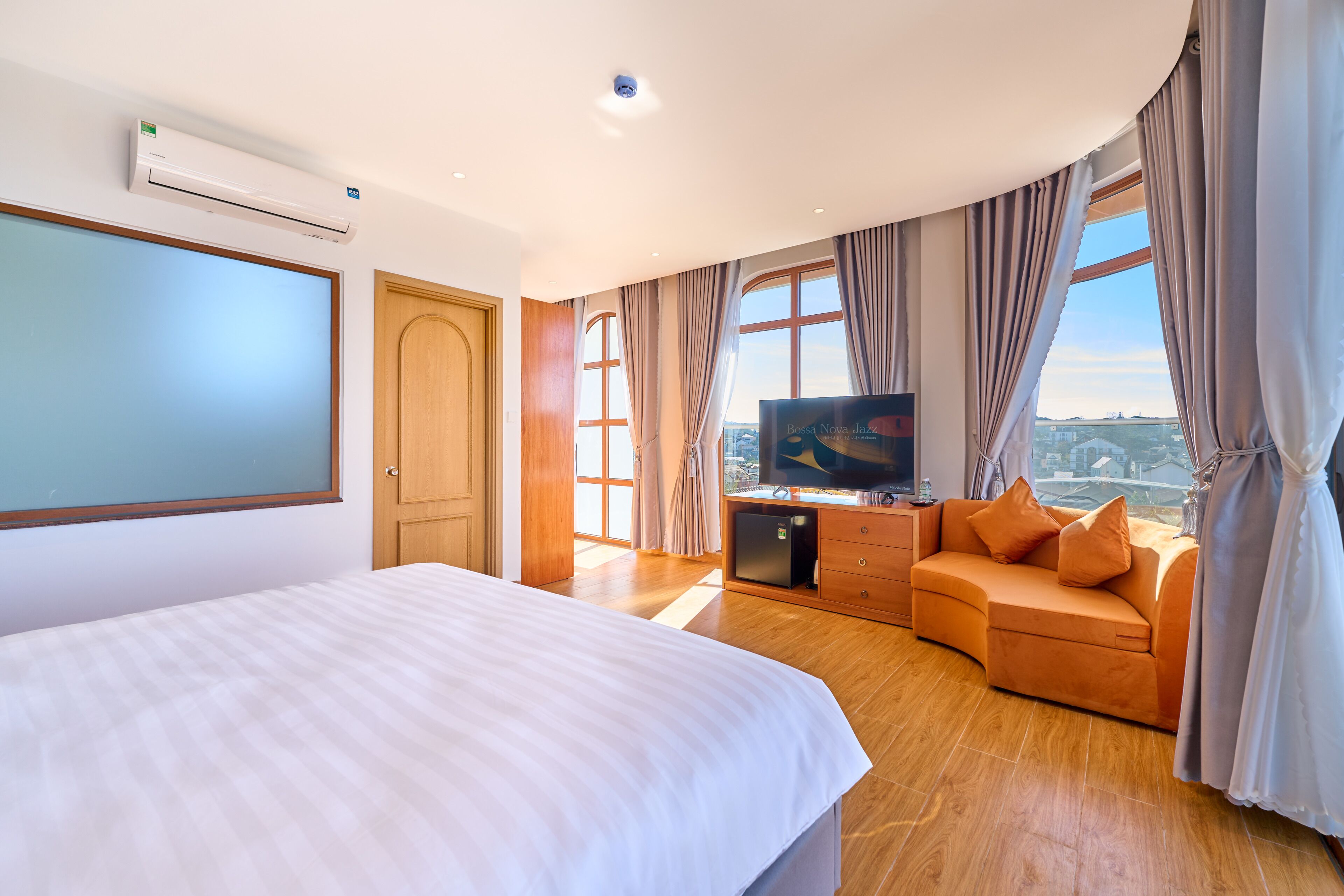 A hotel room with a bed, a TV, a sofa, a small table, and a window with curtains.