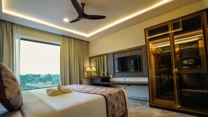 A hotel room with a bed, a desk, a television, and a wardrobe. - UVA MANISH (Kundapur)