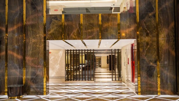 A hotel lobby with a geometric patterned floor, marble walls, and a central staircase. - UVA MANISH (Kundapur)