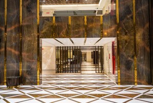 A hotel lobby with a geometric patterned floor, marble walls, and a central staircase.