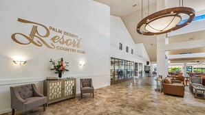 A spacious lobby with a high ceiling, a large chandelier, and a sign reading "Palm Desert Resort Country Club".