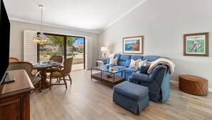 A spacious living room with a blue sofa, a coffee table, and a dining area with chairs and a table.